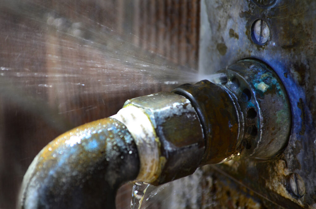 Old rusty pipe with leak and water spraying out- prevent burst pipes
