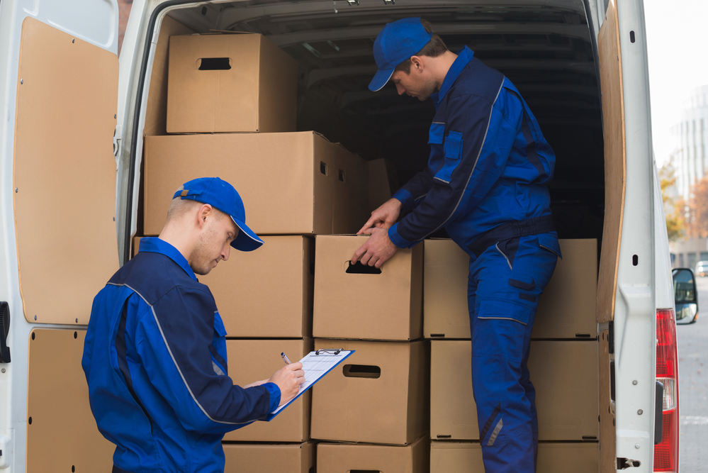 Man unloading cardboard boxes from truck while coworker writing on clipboard